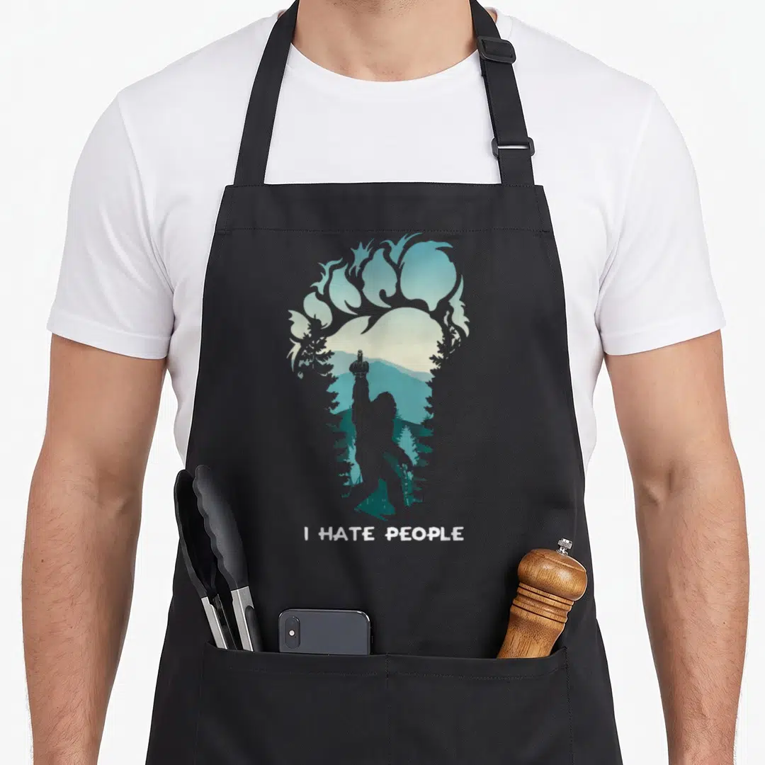 Hate bigfoot apron - I HATE PEOPLE text below a footprint silhouette filled with a teal mountain landscape and a person — shown on a black cotton canvas apron against a white background