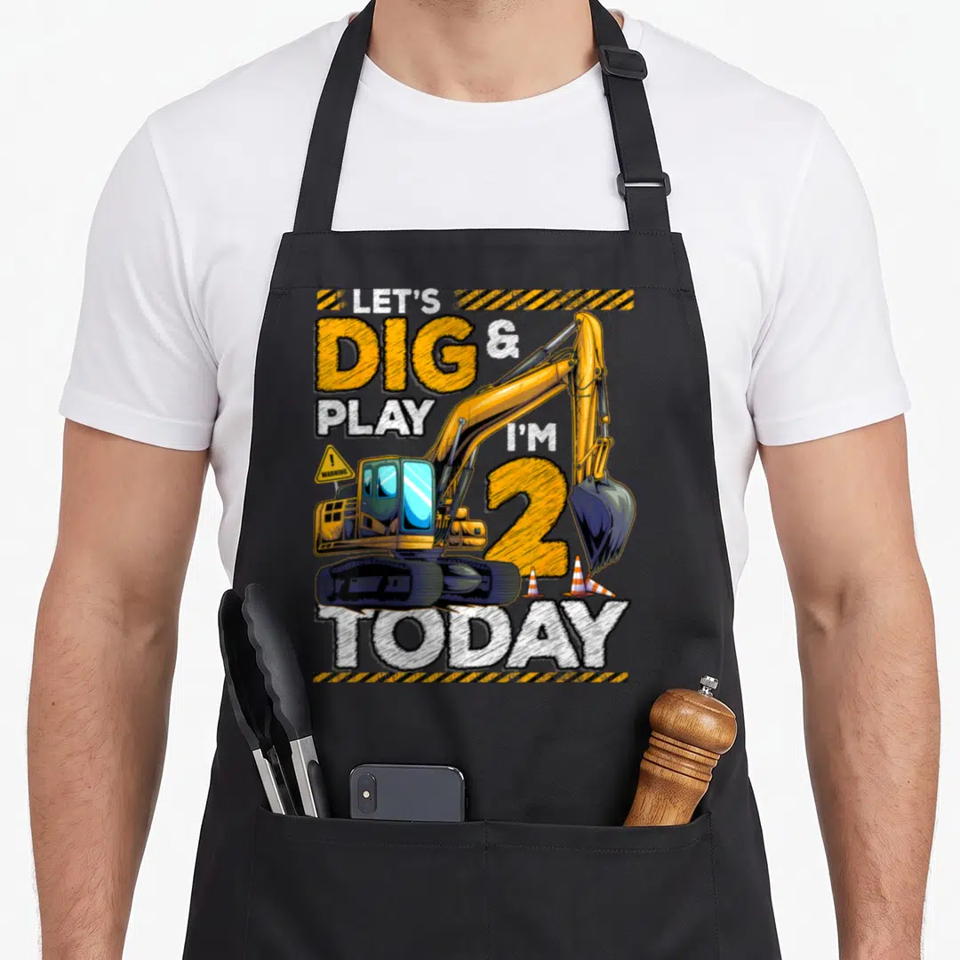 Construction 2nd apron - Yellow excavator with LET'S DIG & PLAY I'M 2 TODAY text and traffic cones — shown on a black cotton canvas apron against a white background
