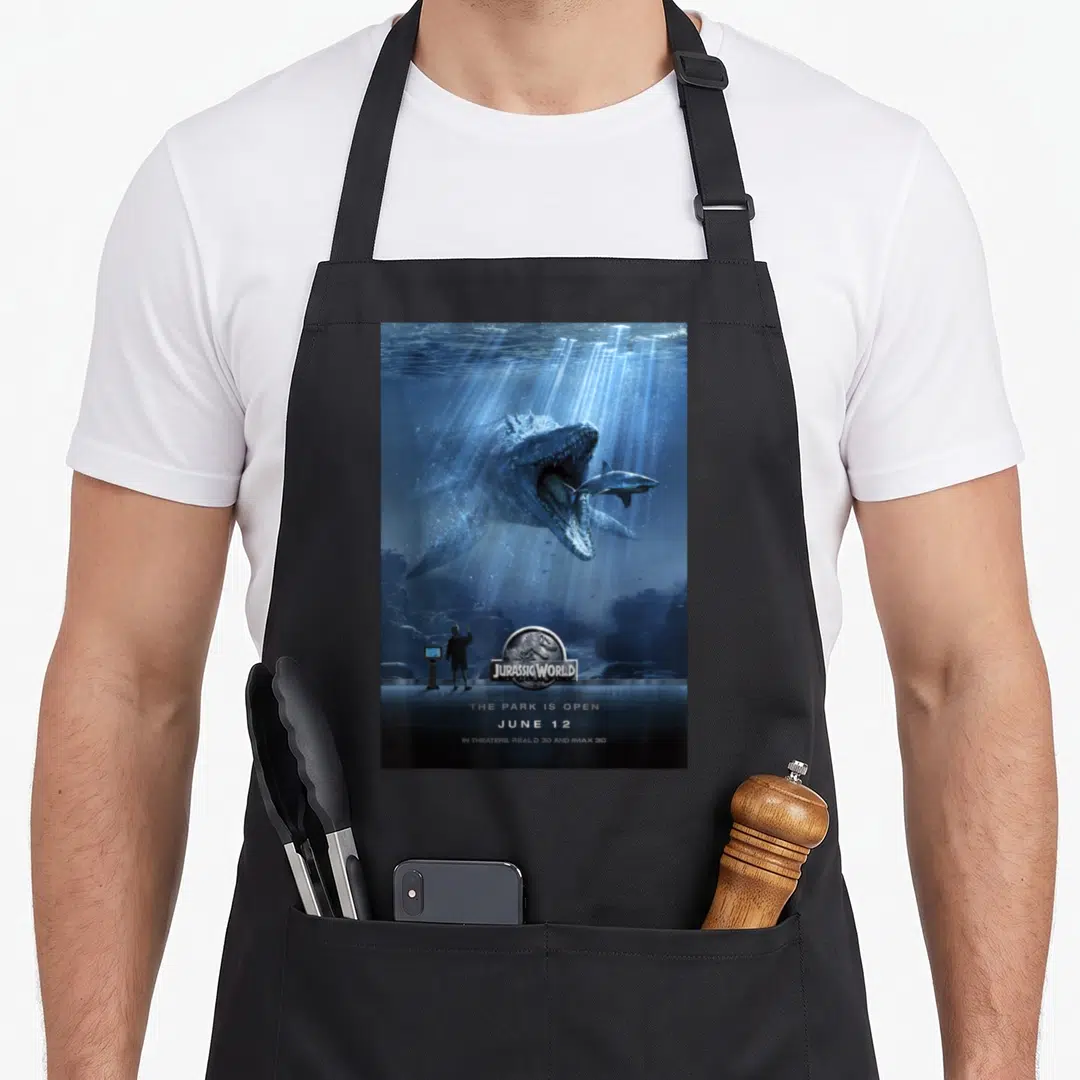 Mosasaurus jurassic world apron - Blue underwater poster with dinosaur eating shark and text Jurassic World The Park Is — shown on a black cotton canvas apron against a white background