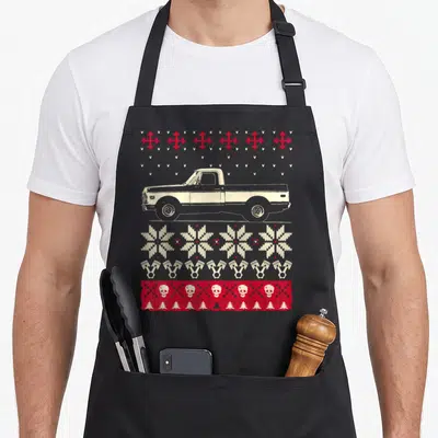 Pickup ugly christmas sweater apron - Beige pickup truck with red snowflakes, beige pistons, skulls, and pine tree rows — shown on a black cotton canvas apron against a white background