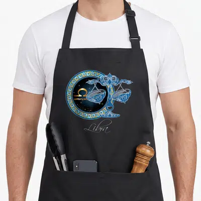Beautifully zodiac aprons - Blue and gold Libra scales over circular zodiac frame with stars and script text — shown on a black cotton canvas apron against a white background