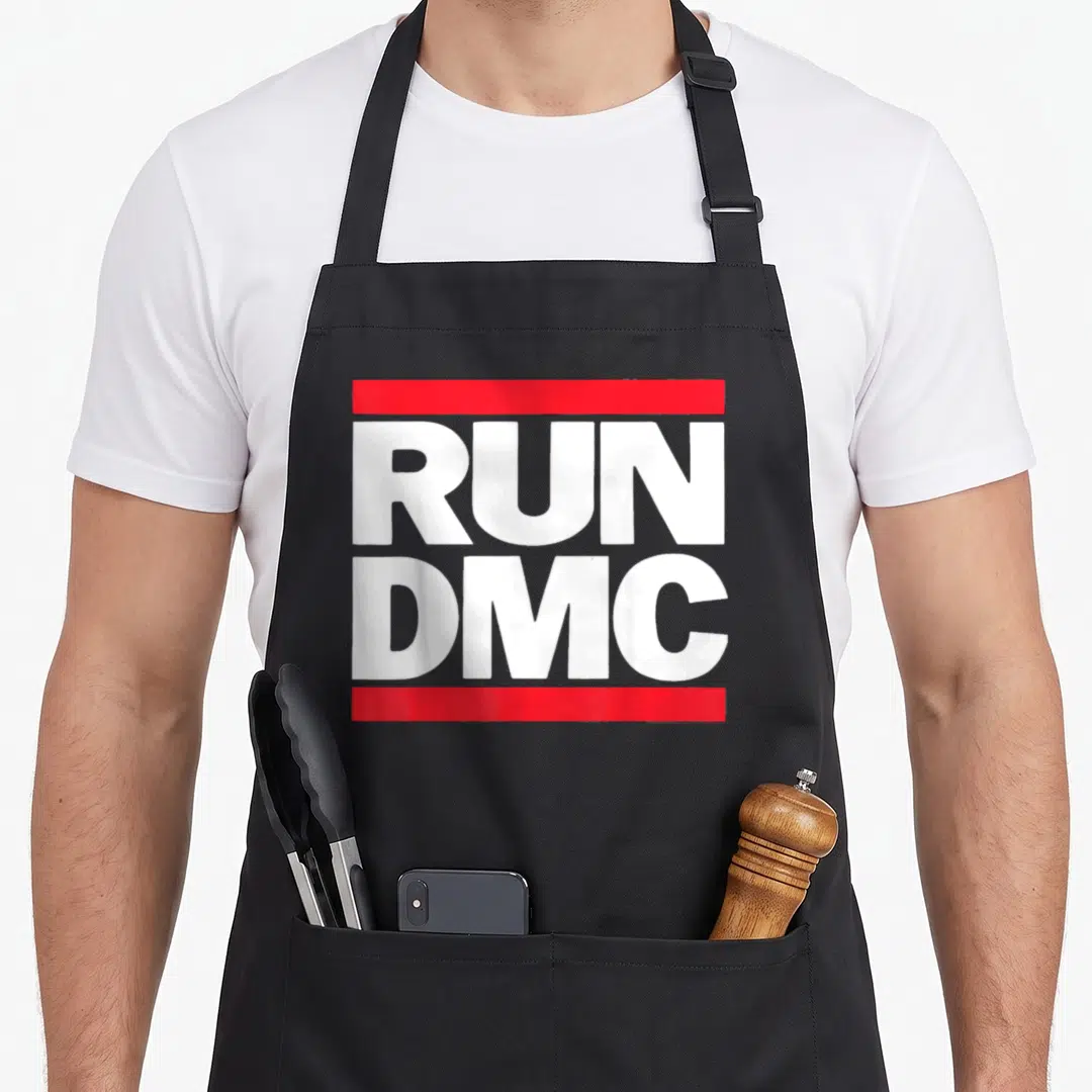 Run novelty apron - White RUN DMC text between two red horizontal bars — shown on a black cotton canvas apron against a white background