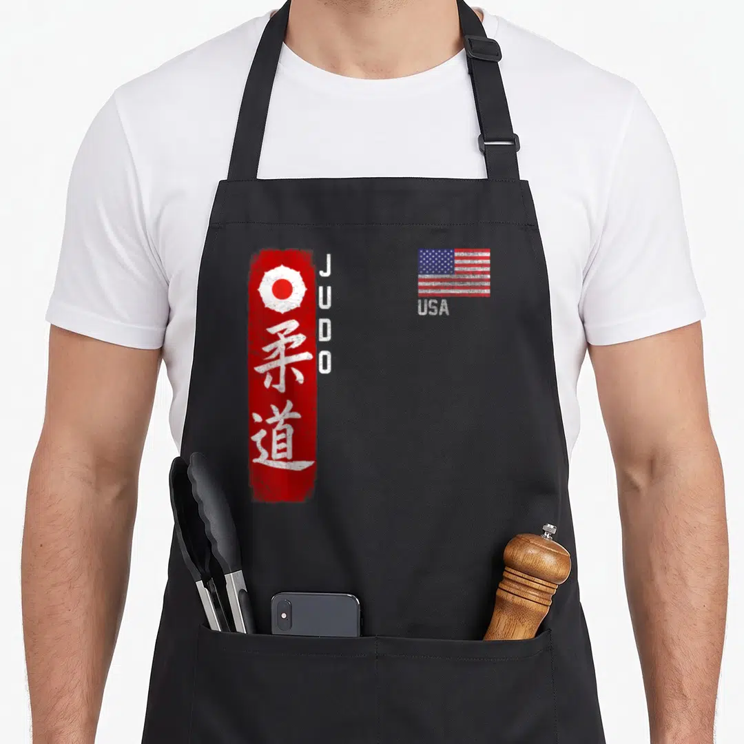 Judo american flag apron - Red brushstroke with white kanji and JUDO text beside a distressed USA flag — shown on a black cotton canvas apron against a white background