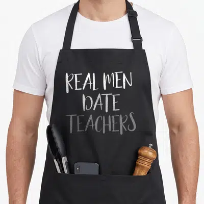 Date teacher pocket apron - White stacked text reading REAL MEN DATE TEACHERS on grey background — shown on a black cotton canvas apron against a white background
