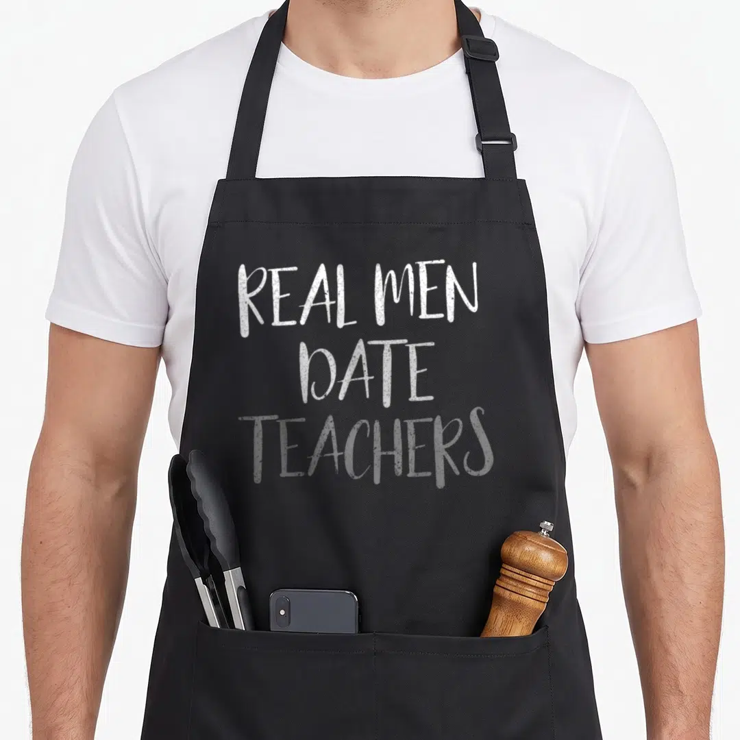 Date teacher pocket apron - White stacked text reading REAL MEN DATE TEACHERS on grey background — shown on a black cotton canvas apron against a white background