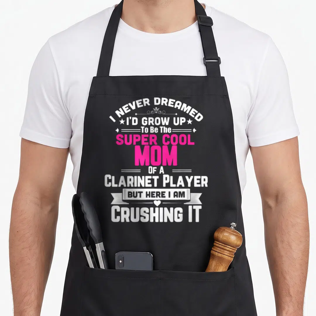 Player pipe mom apron - Stacked white and pink text reading Super Cool Mom Of A Clarinet Player with decorative stars — shown on a black cotton canvas apron against a white background