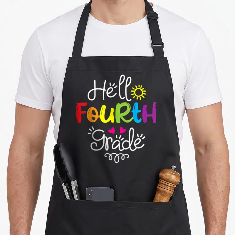 Fourth hello apron - Hello FOURTH Grade rainbow text with yellow sun and two pink hearts in cartoon style — shown on a black cotton canvas apron against a white background