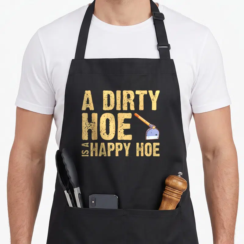Dirty gardener apron - Distressed text A DIRTY HOE IS A HAPPY HOE with an orange handle blue blade hoe graphic — shown on a black cotton canvas apron against a white background
