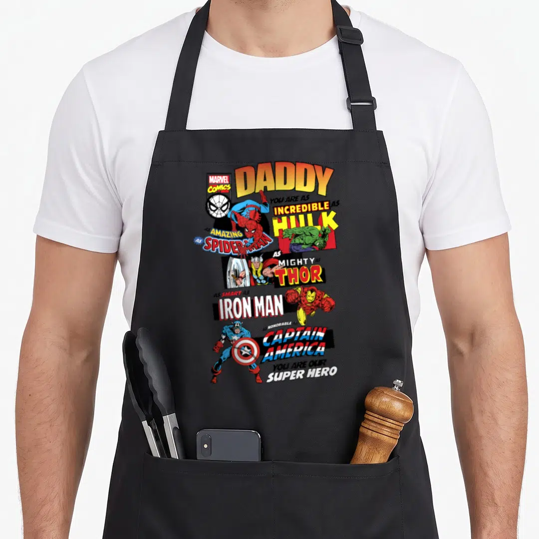 Comic father day apron - Vertical stack of cartoon superheroes with DADDY text in orange, yellow, red, blue, green — shown on a black cotton canvas apron against a white background