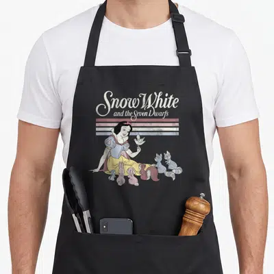 Critter snow white apron - Retro Snow White graphic with animals below three colored stripes and stacked script text — shown on a black cotton canvas apron against a white background
