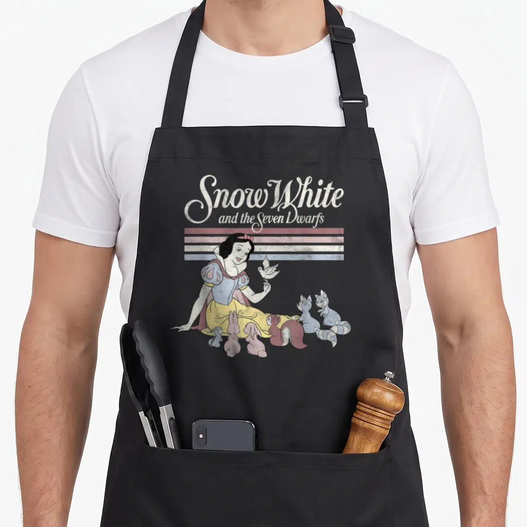 Critter snow white apron - Retro Snow White graphic with animals below three colored stripes and stacked script text — shown on a black cotton canvas apron against a white background