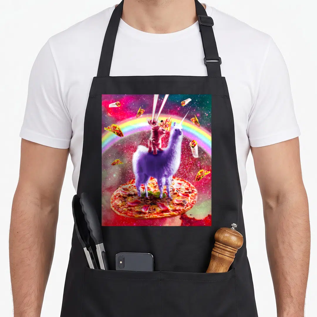 Eye space cat apron - Purple llama on pizza with laser-eyed cat and floating tacos in rainbow space — shown on a black cotton canvas apron against a white background