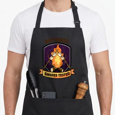 Tester camping apron - Purple shield campfire design with marshmallows and official smores tester text — shown on a black cotton canvas apron against a white background