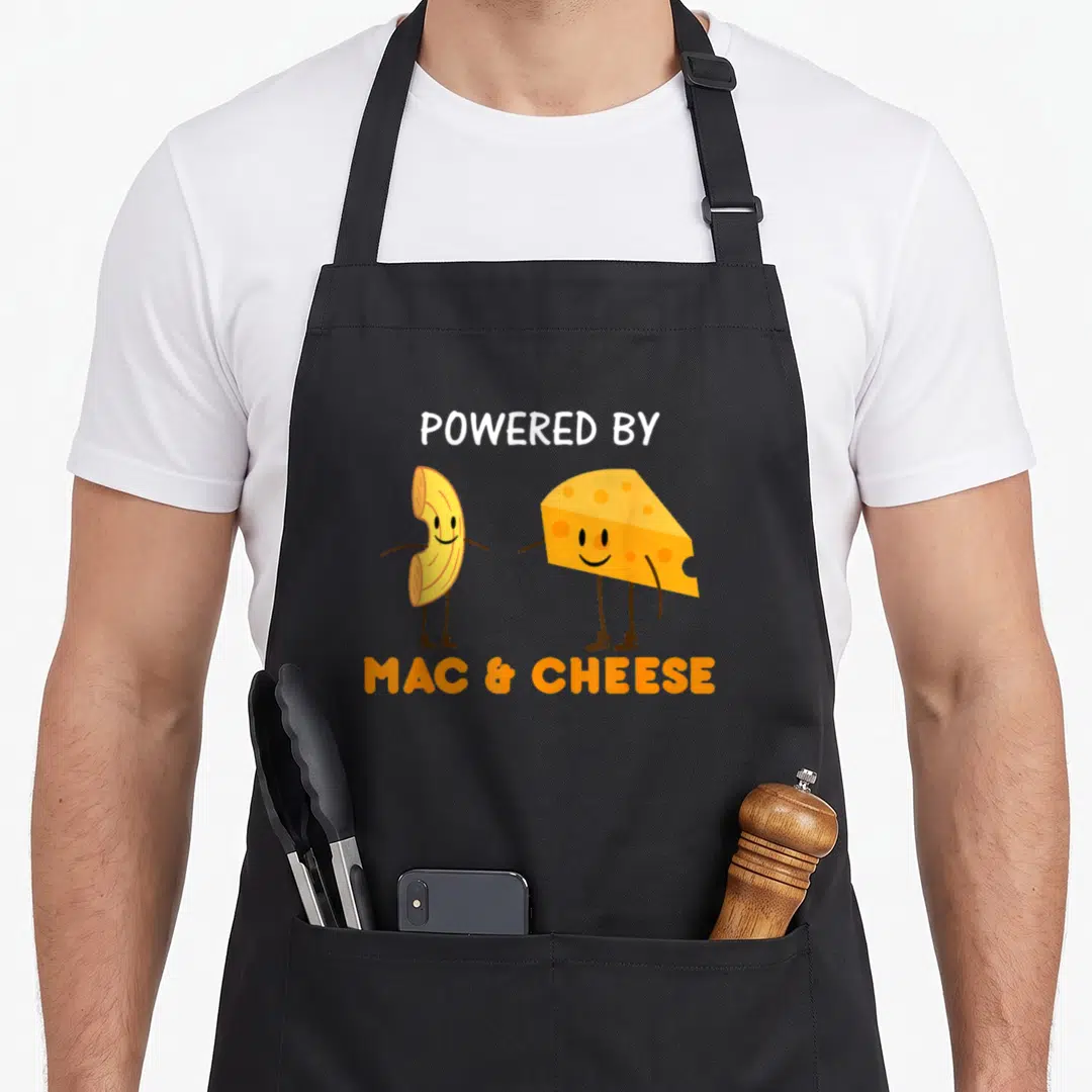 Powered cheese mac apron - Cartoon macaroni noodle and cheese wedge standing side by side with POWERED BY MAC & CHEESE — shown on a black cotton canvas apron against a white background
