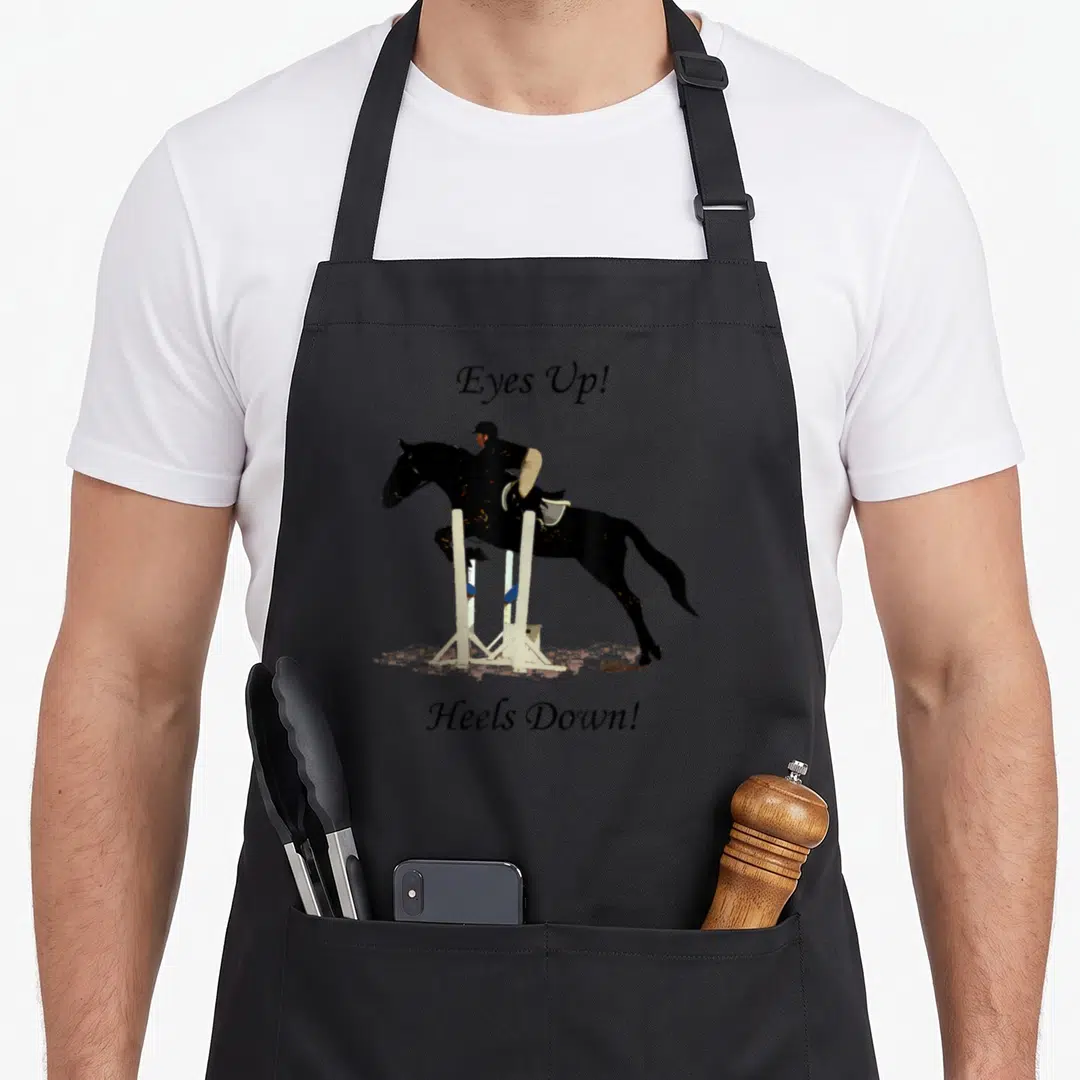 Eye horse apron - Black horse jumping white fence with Eyes Up Heels Down text — shown on a black cotton canvas apron against a white background