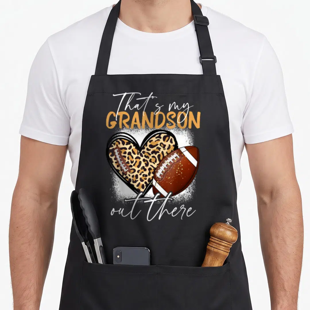 Grandson proud grandma aprons - Leopard heart and brown football with That's my GRANDSON out there text — shown on a black cotton canvas apron against a white background