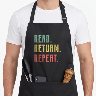 Read learn today apron - Stacked text READ RETURN REPEAT in green yellow red distressed font — shown on a black cotton canvas apron against a white background