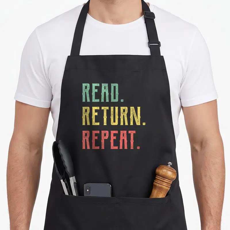 Read learn today apron - Stacked text READ RETURN REPEAT in green yellow red distressed font — shown on a black cotton canvas apron against a white background