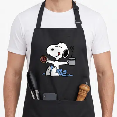 Donut coffee apron - White cartoon dog holding pink donut and grey mug with blue blanket — shown on a black cotton canvas apron against a white background