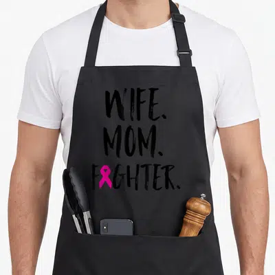 Mother wife breast cancer awareness aprons - Stacked WIFE. MOM. FIGHTER. text with pink ribbon replacing the I — shown on a black cotton canvas apron against a white background