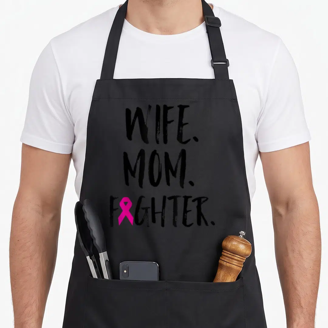 Mother wife breast cancer awareness aprons - Stacked WIFE. MOM. FIGHTER. text with pink ribbon replacing the I — shown on a black cotton canvas apron against a white background