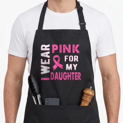 Daughter breast cancer awareness aprons - I WEAR PINK FOR MY DAUGHTER text with pink ribbon and distressed white letters — shown on a black cotton canvas apron against a white background