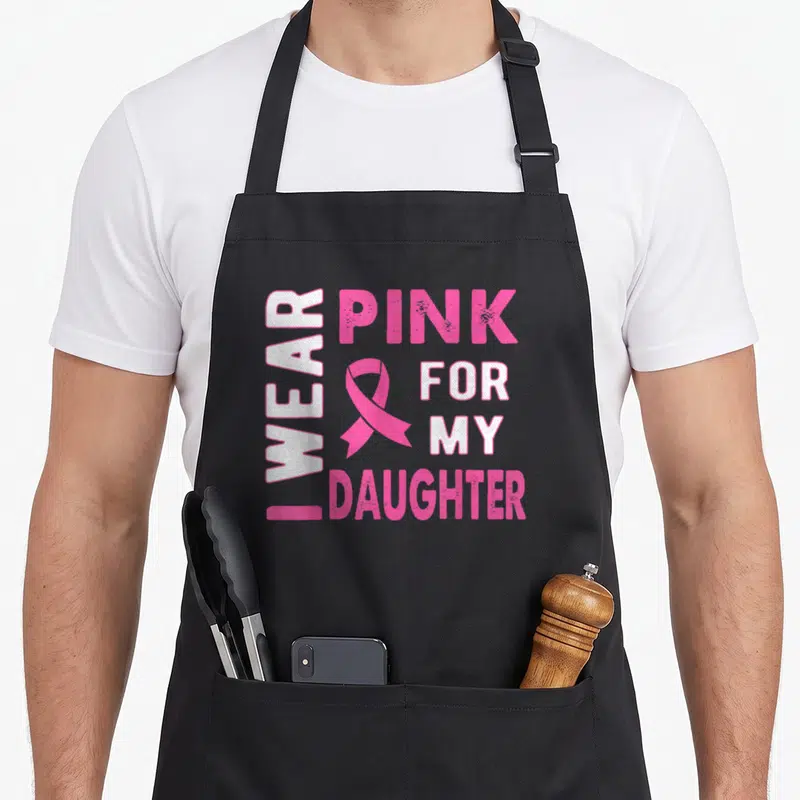 Daughter breast cancer awareness aprons - I WEAR PINK FOR MY DAUGHTER text with pink ribbon and distressed white letters — shown on a black cotton canvas apron against a white background