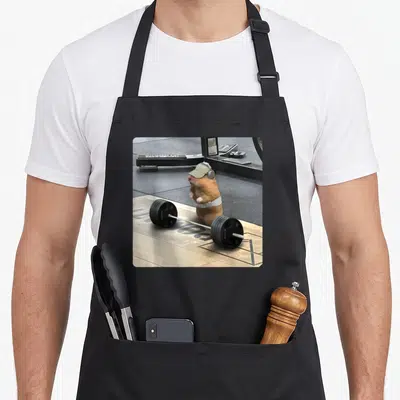 Deadlift meme apron - Hamster wearing cap and belt standing behind barbell in gym setting — shown on a black cotton canvas apron against a white background