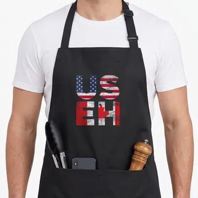 Useh american flag apron - Stacked US and EH text filled with distressed American flag and Canadian maple leaf patterns — shown on a black cotton canvas apron against a white background
