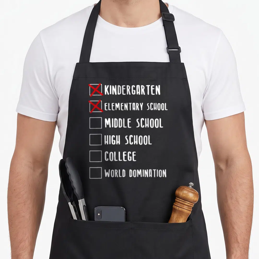 Funny middle school graduation apron - Checklist with red Xs over Kindergarten and Elementary School text leading — shown on a black cotton canvas apron against a white background