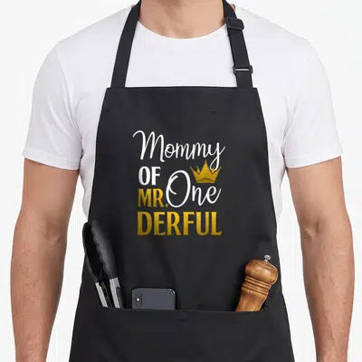 Onederful mother's day aprons - Stacked white and gold text reading Mommy OF MR. One DERFUL with gold crown above One — shown on a black cotton canvas apron against a white background