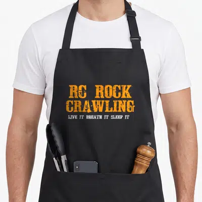 Funny crawler girl apron - Orange and white distressed typography reading RC Rock Crawling Live It Breath It Sleep It — shown on a black cotton canvas apron against a white background