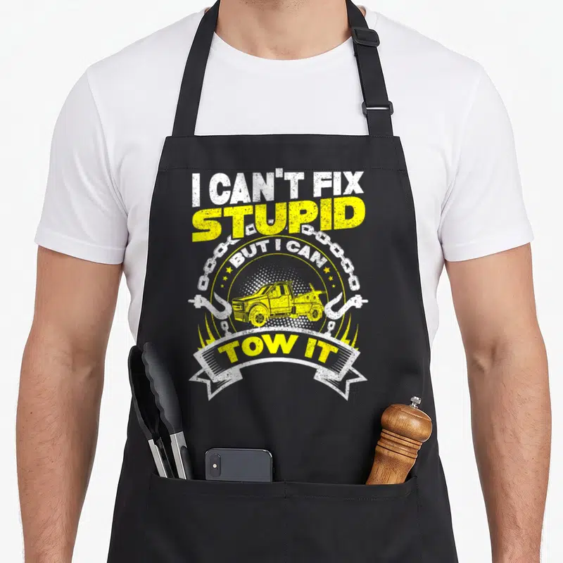 Tow truck apron - Yellow tow truck graphic with chain hooks and sarcastic text in distressed font — shown on a black cotton canvas apron against a white background