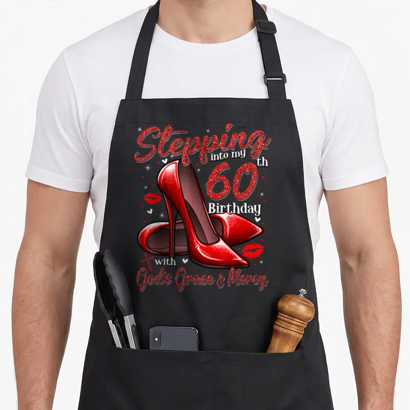Heel stepping 60th birthday apron - Red high heels and Stepping into my th 60 Birthday with God's Grace & Mercy text — shown on a black cotton canvas apron against a white background