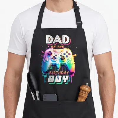 Birthday video game apron for men - Multicolored dripping game controller between Dad of the Birthday Boy text — shown on a black cotton canvas apron against a white background