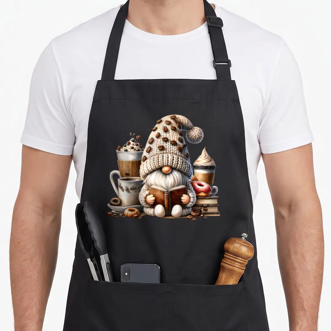 Latte coffee apron - Cartoon gnome reading book flanked by coffee cups and donuts in beige and brown — shown on a black cotton canvas apron against a white background