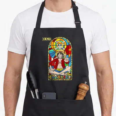 Anime stained apron - Monkey D. Luffy in stained glass window with ONE PIECE text and skull emblem — shown on a black cotton canvas apron against a white background