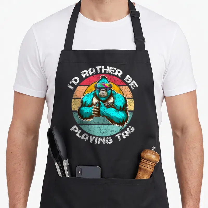 Rather tag apron - Teal gorilla VR headset controller retro striped sunset white distressed text — shown on a black cotton canvas apron against a white background