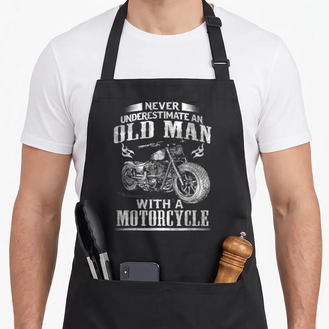 Underestimate motorcycle apron - White distressed motorcycle graphic flanked by flames with stacked sarcastic text — shown on a black cotton canvas apron against a white background