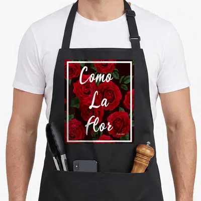 Como rose apron - Red roses and green leaves with stacked white Como La Flor text inside white border on black — shown on a black cotton canvas apron against a white background