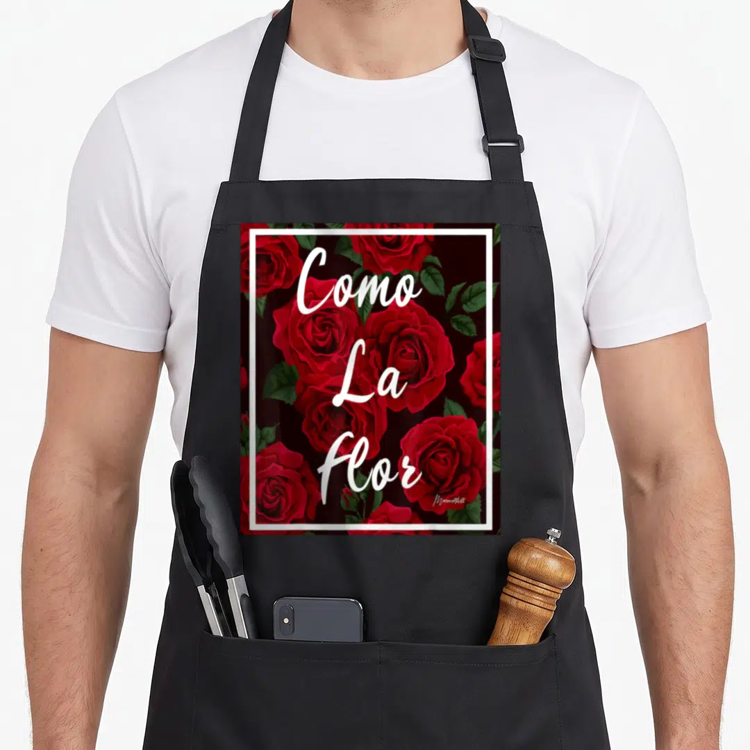 Como rose apron - Red roses and green leaves with stacked white Como La Flor text inside white border on black — shown on a black cotton canvas apron against a white background
