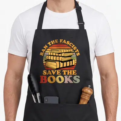 Fascist nerd apron - Retro stack of four books with striped sun background and slogan Ban The Fascists Save The Books — shown on a black cotton canvas apron against a white background