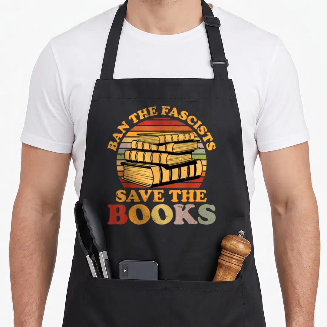 Fascist nerd apron - Retro stack of four books with striped sun background and slogan Ban The Fascists Save The Books — shown on a black cotton canvas apron against a white background