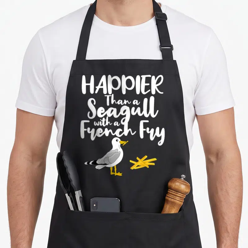 Summer french apron - Cartoon seagull holding yellow french fry under stacked white text on grey background — shown on a black cotton canvas apron against a white background