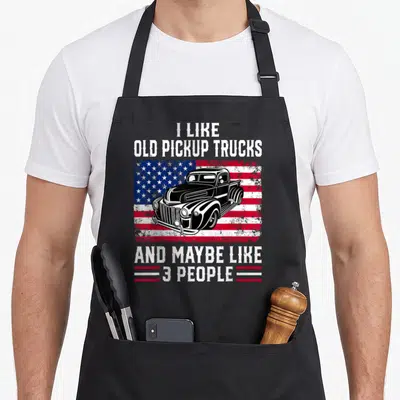 Pickup american flag apron - Black vintage truck on distressed flag with white text I like old pickup trucks and maybe — shown on a black cotton canvas apron against a white background