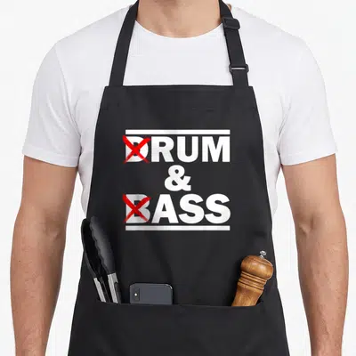 Drum bass apron - Stacked white text DRUM & BASS with red crosses over D and B and white horizontal lines — shown on a black cotton canvas apron against a white background