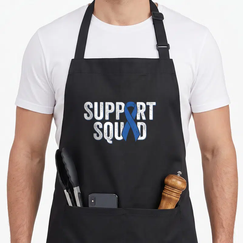 Colon ribbon apron - SUPPORT SQUAD text with vertical blue ribbon overlapping letters in distressed white font — shown on a black cotton canvas apron against a white background