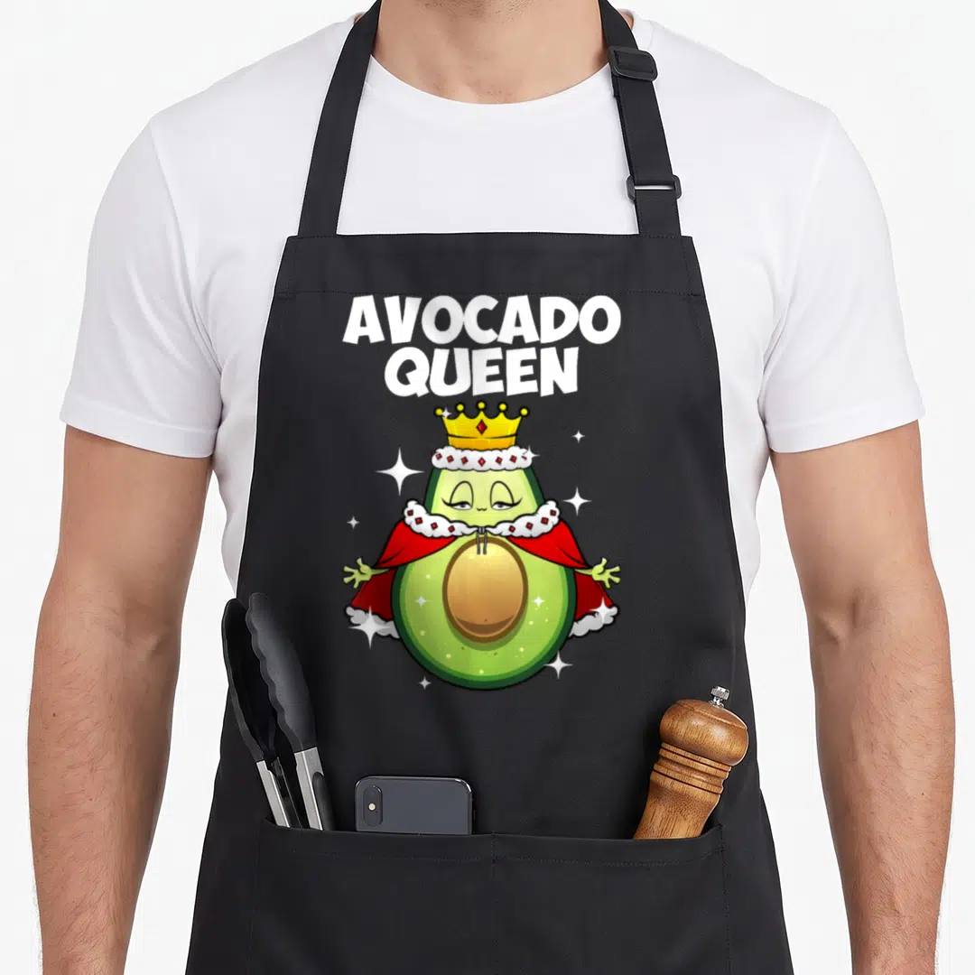Funny queen avocado apron - Arched AVOCADO QUEEN text above cartoon avocado wearing gold crown and red cape with white — shown on a black cotton canvas apron against a white background