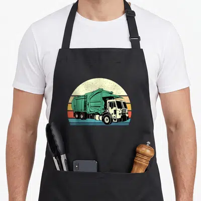 Garbage dump truck apron - Teal garbage truck centered on retro sun with orange and yellow horizontal stripes — shown on a black cotton canvas apron against a white background