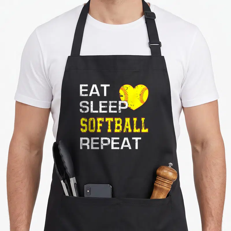 Softball catcher apron - EAT SLEEP SOFTBALL REPEAT text with yellow heart softball graphic — shown on a black cotton canvas apron against a white background